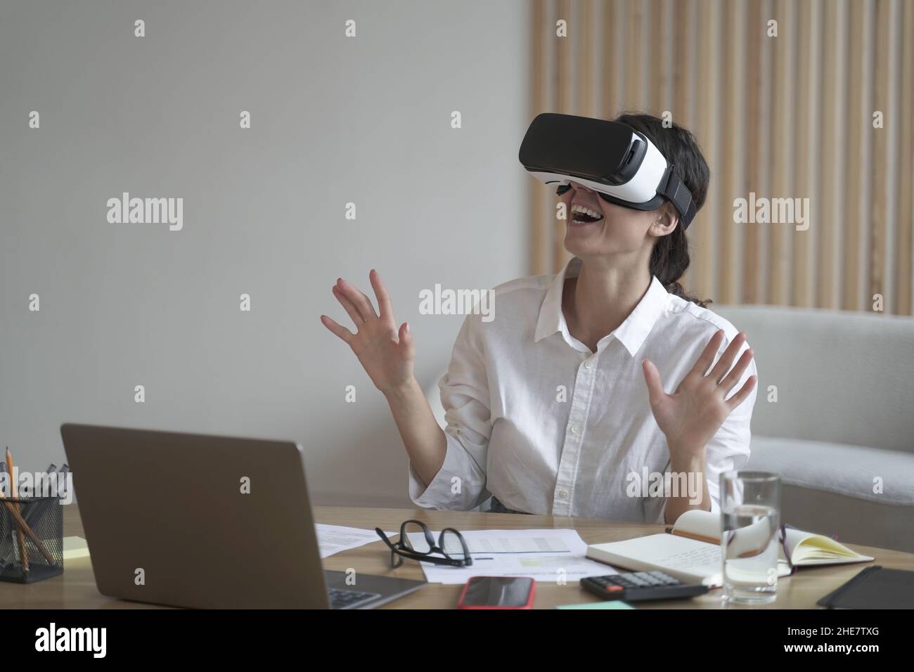 Business lady wears VR headset for laptop raising hands up as trying to touch objects in 3D reality Stock Photo