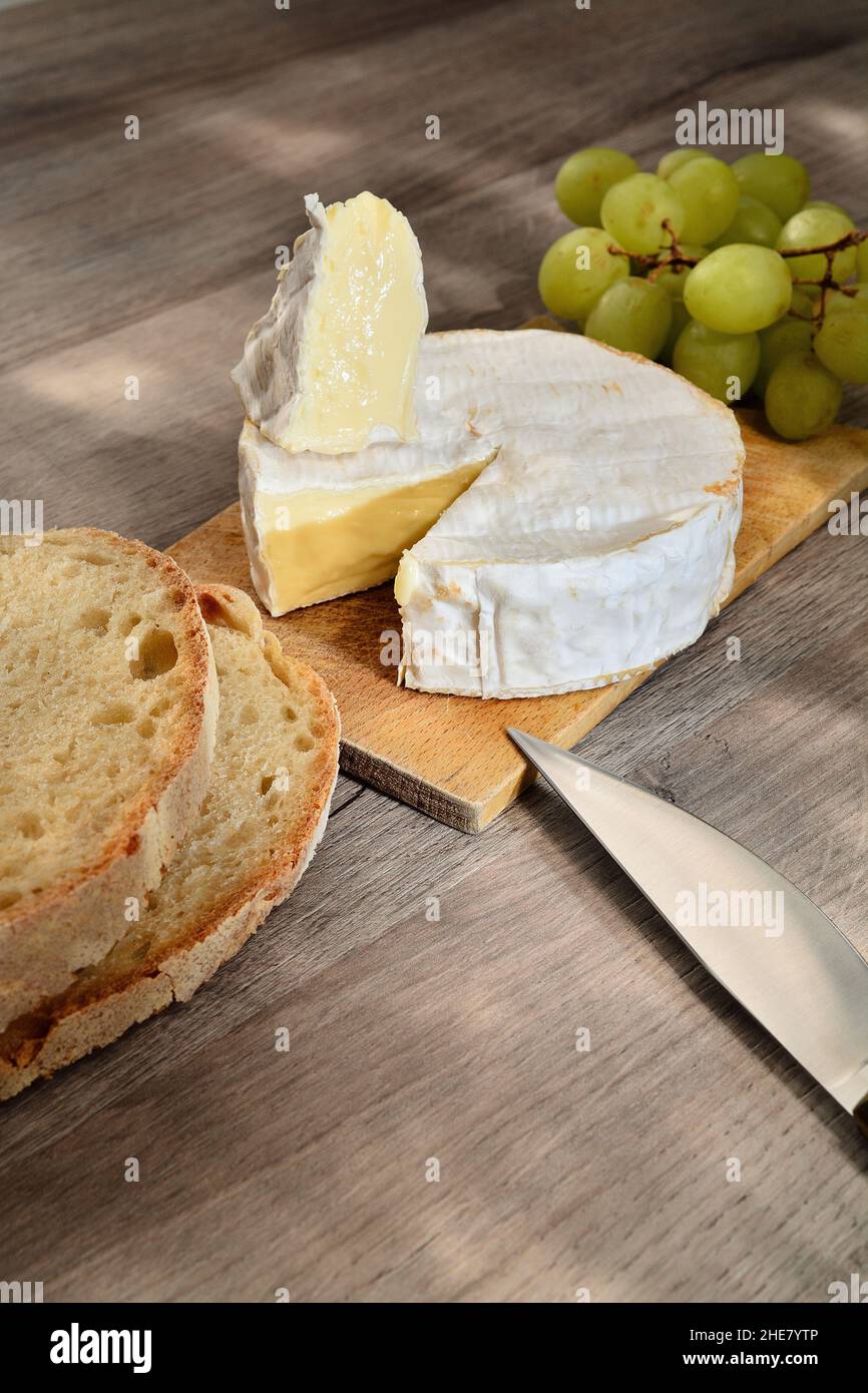 French camembert of Normandy served on wooden cutting board with grapes and slices of bread. Stock Photo