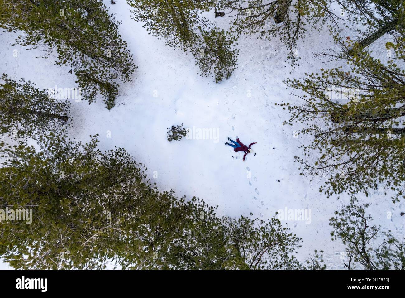 Drone aerial of woman wearing warm clothing lie down at snow in winter. Troodos cyprus Stock Photo
