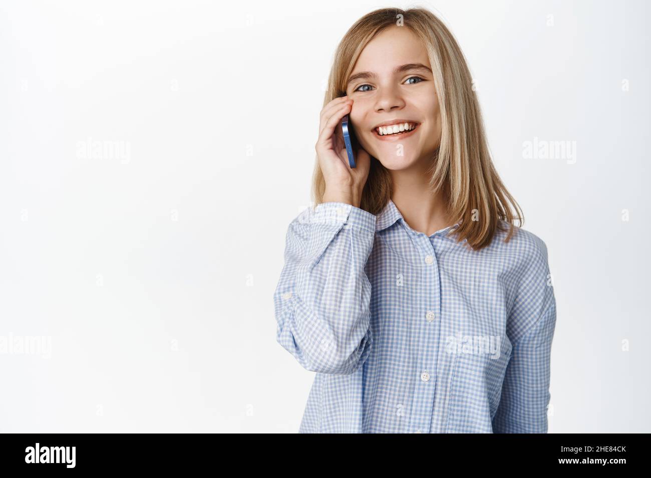 Cute little girl, beautiful blond kid talking on mobile phone, having conversation on smartphone, answer a call, standing over white background Stock Photo