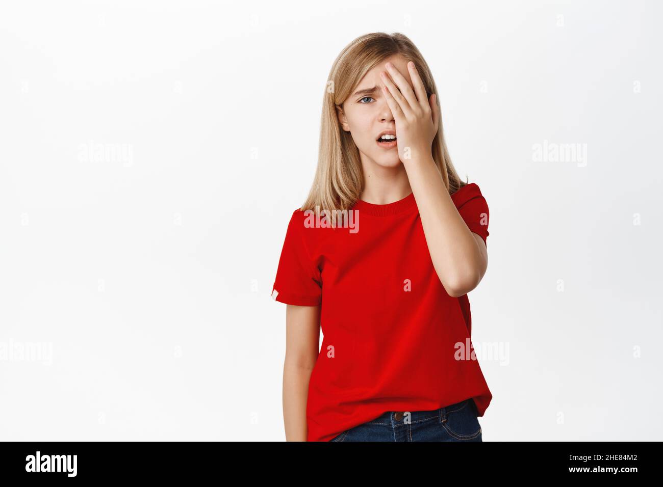 Little girl looks upset and gloomy, facepalm, sighing and frowning disappointed, troubled of failure, losing, standing over white background in red Stock Photo