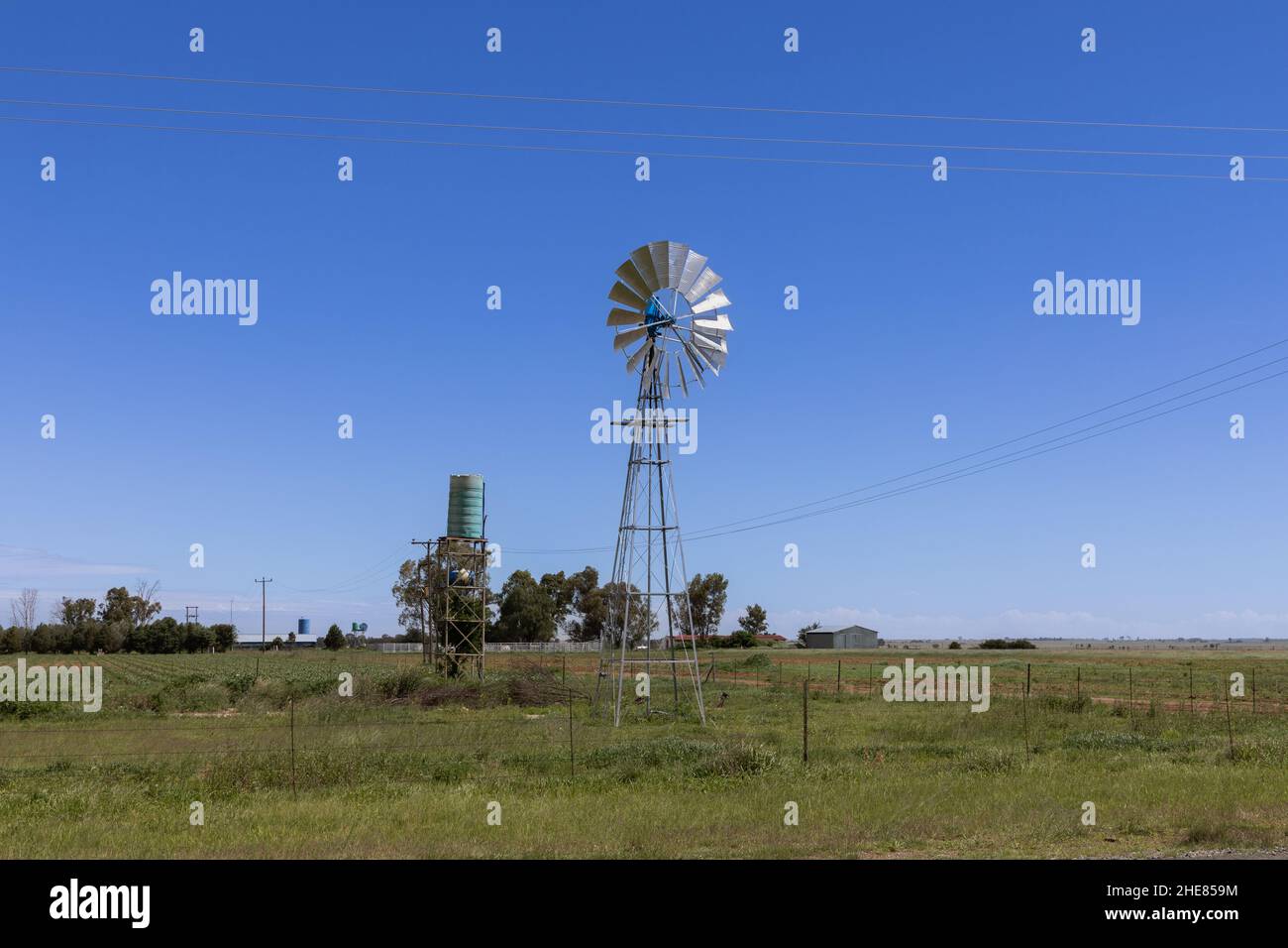 Wind pump also known as a wind mill in a rural area, being it is a green plastic storage tank to contain the water that is extracted from the earth Stock Photo