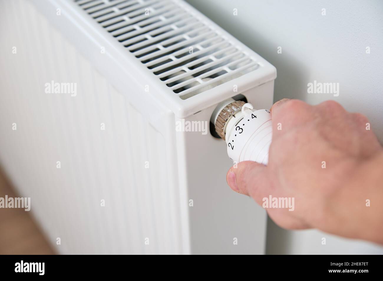 Hand adjusting temperature on heating radiator thermostat, Turning heat radiator knob to control heat in home Stock Photo
