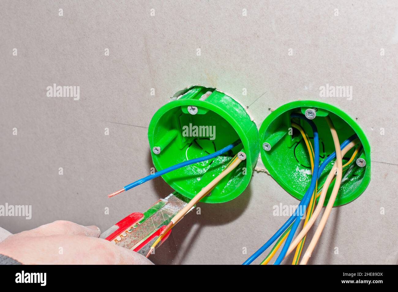 An electrician installs an outlet box into a drywall wall to install an electrical outlet. Home renovation. Stock Photo