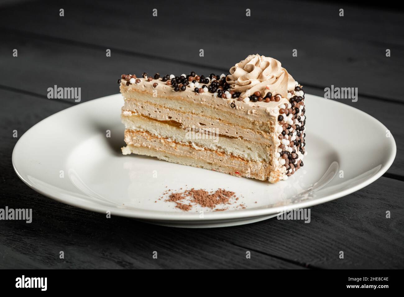 Piece of delicious cake with a flower, sweet balls and cream on a white plate. Stock Photo
