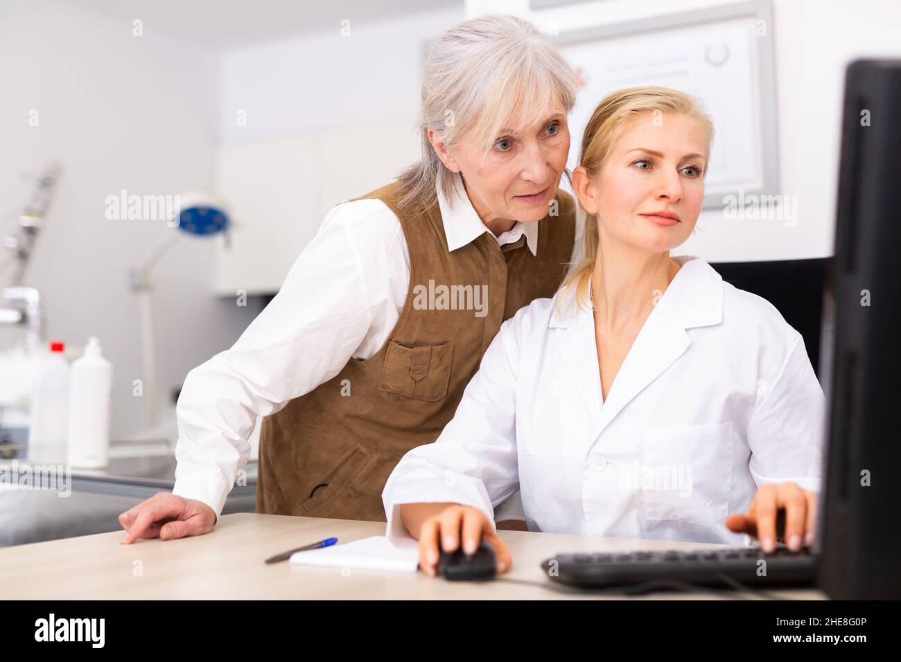 Interested elderly female client with cosmetologist looking at computer screen Stock Photo