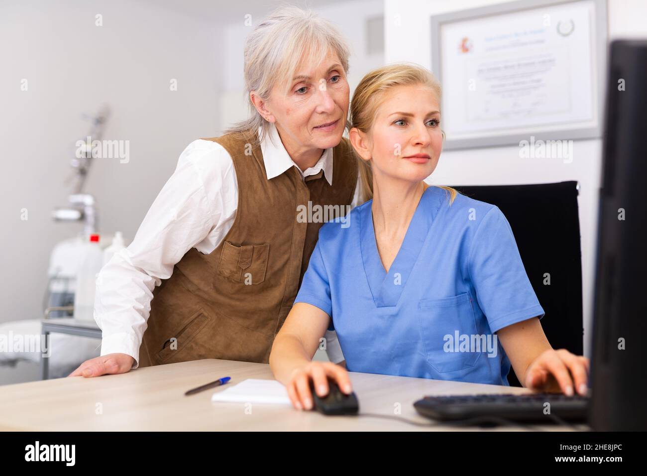 Interested elderly female client with cosmetologist looking at computer screen Stock Photo