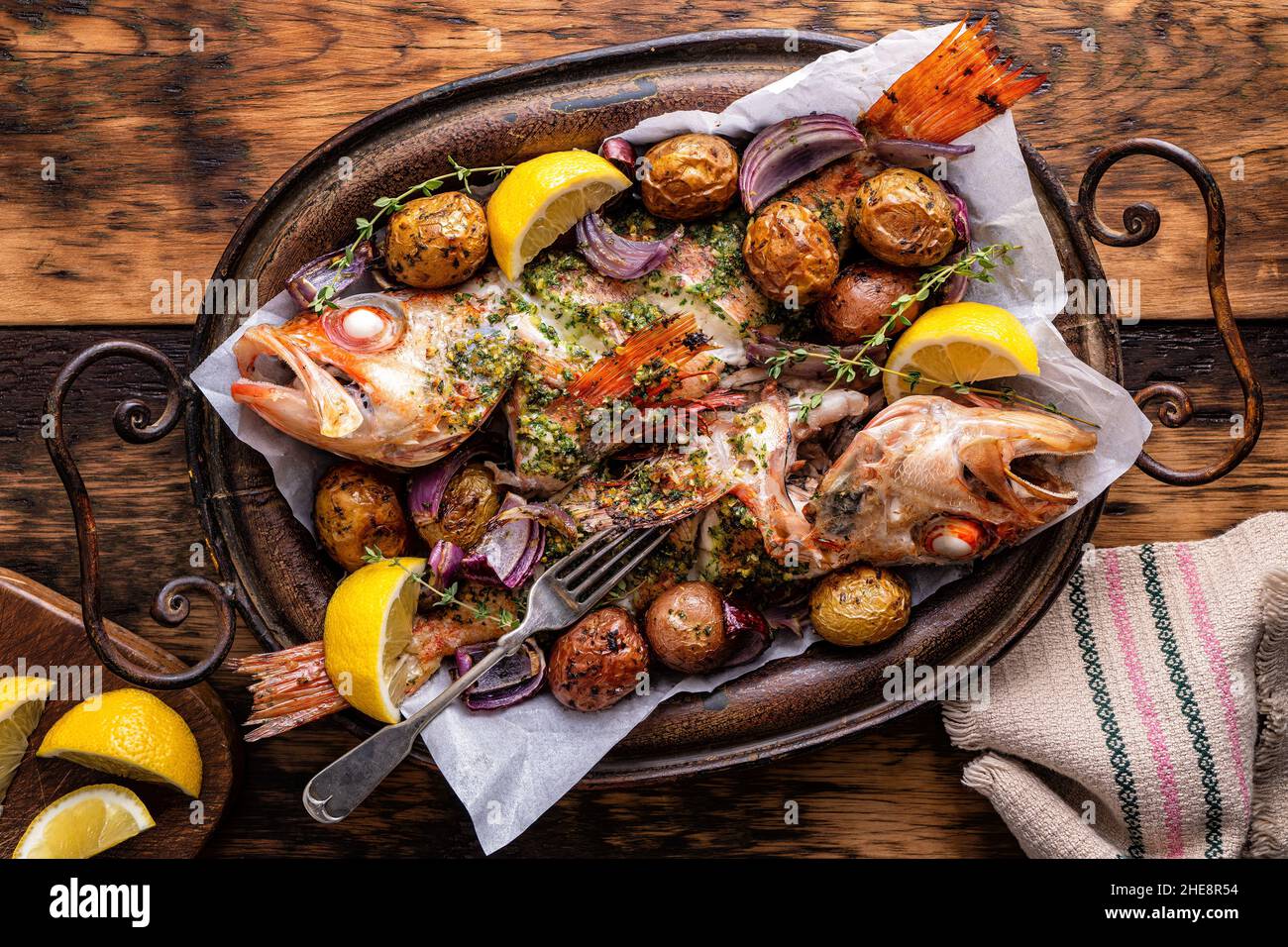 Delicious whole baked redfish with chimichurri sauce, baby potatoes, red onion, lemon and thyme. Stock Photo