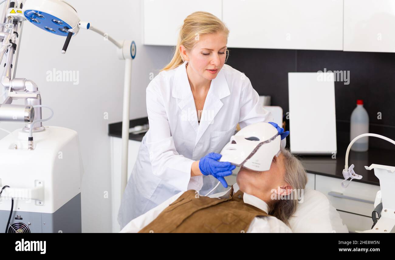 Cosmetologist using spectrum mask on elderly woman Stock Photo - Alamy