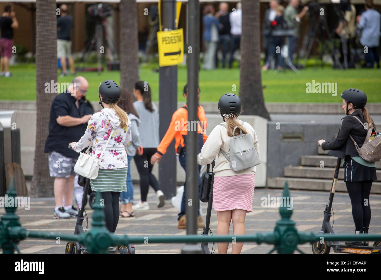 Teenage girls wearing helmets ride their electric battery scooters at circular quay in Sydney city centre,NSW,Australia Stock Photo