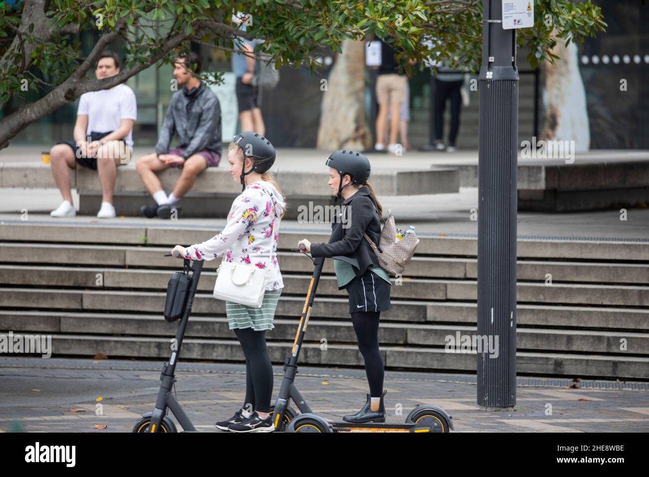 Teenage girls wearing helmets ride their electric battery scooters at circular quay in Sydney city centre,NSW,Australia Stock Photo