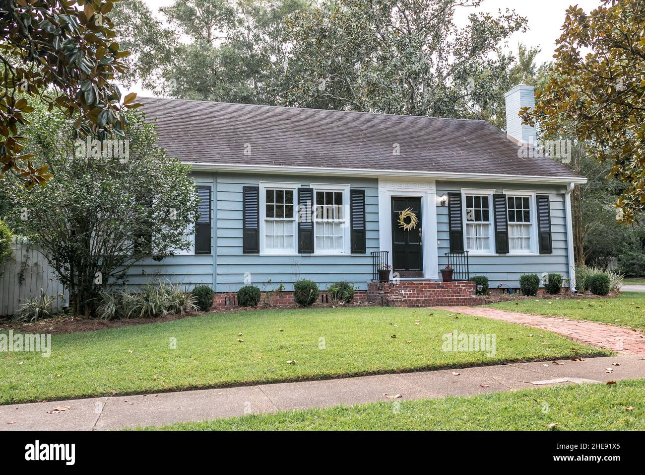 An old blue cottage style small older house with a front lawn and sidewalk Stock Photo