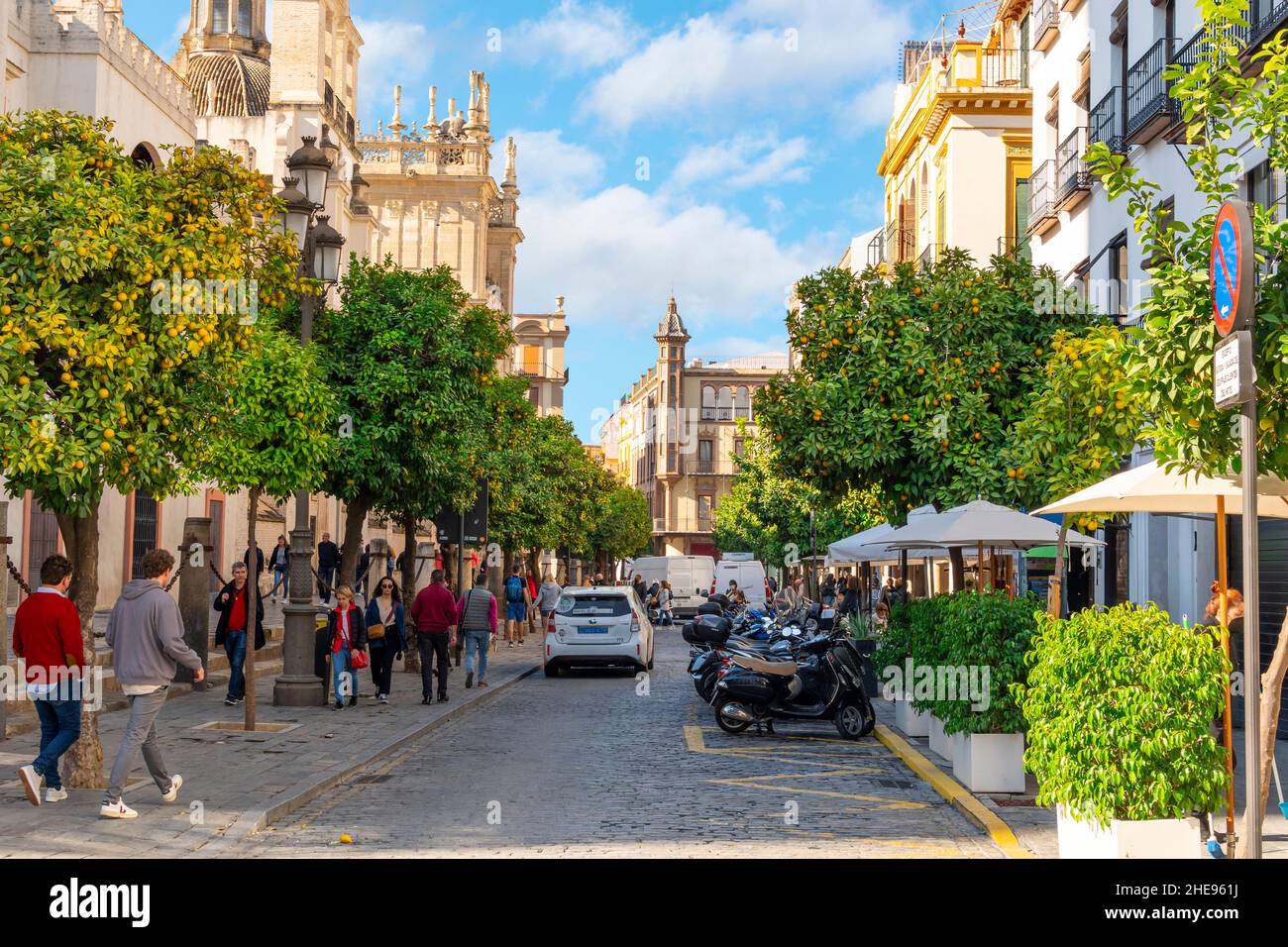 A busy street of cafes and orange trees next to the Great Cathedral of Seville on a sunny autumn day as tourists and Spaniards walk on the sidewalk. Stock Photo