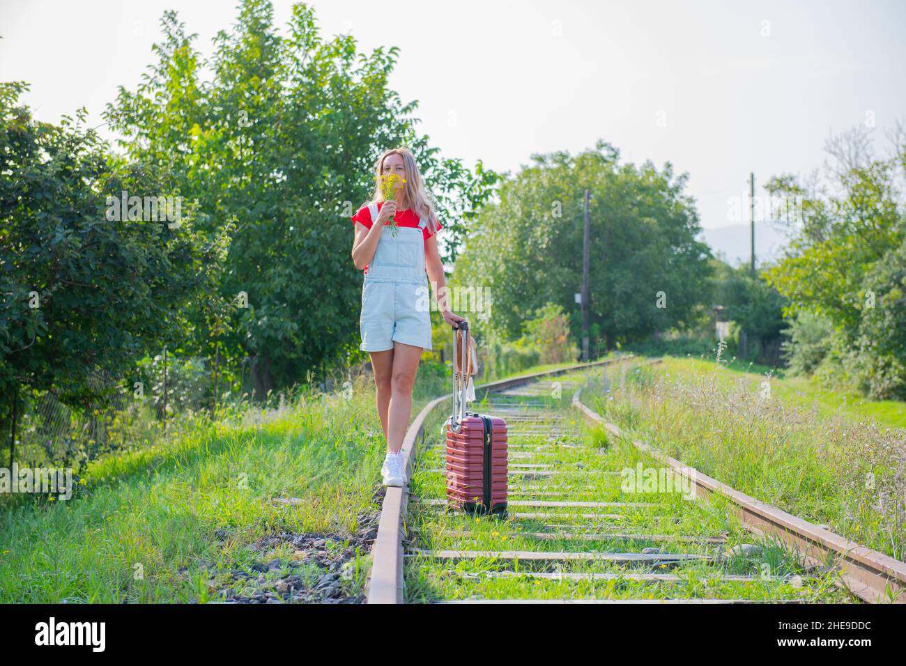 naughty woman with a hat walks on the rails with a suitcase Stock Photo