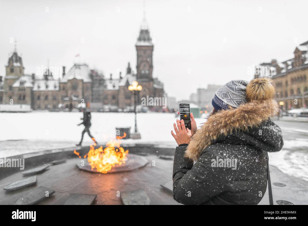 Ottawa travel tourist woman taking photo with phone of Canadian Parliament in Ontario, Canada. Snowing landscape and centennial flame that do not Stock Photo