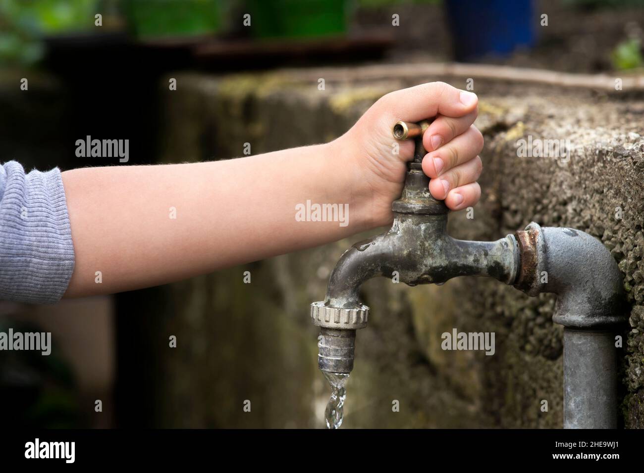 Hand from a child is turning tap water valve and letting water out. Stock Photo