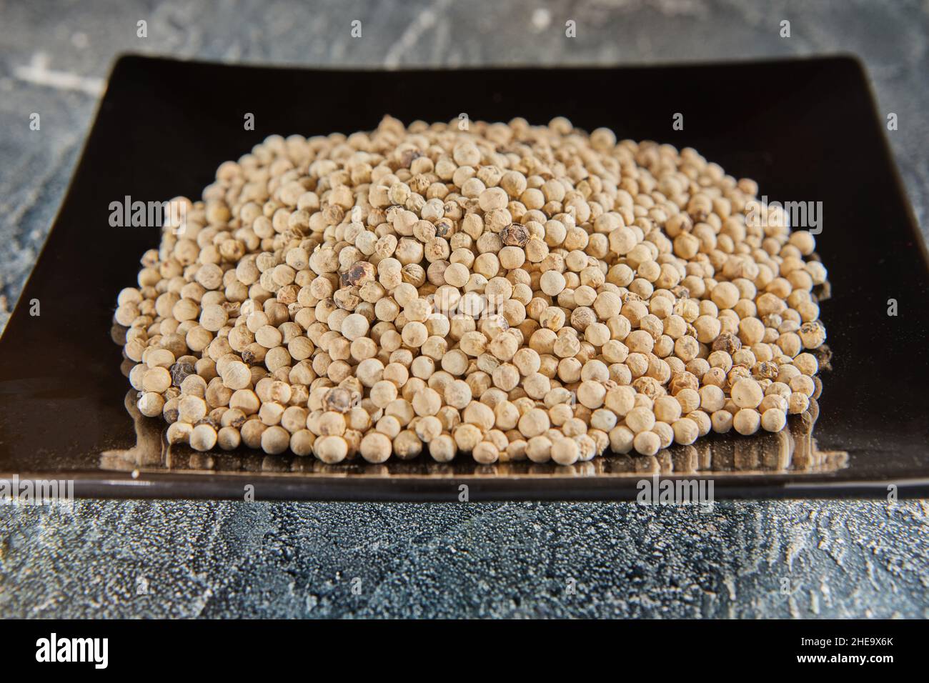 White peppercorns on black plate with reflection Stock Photo