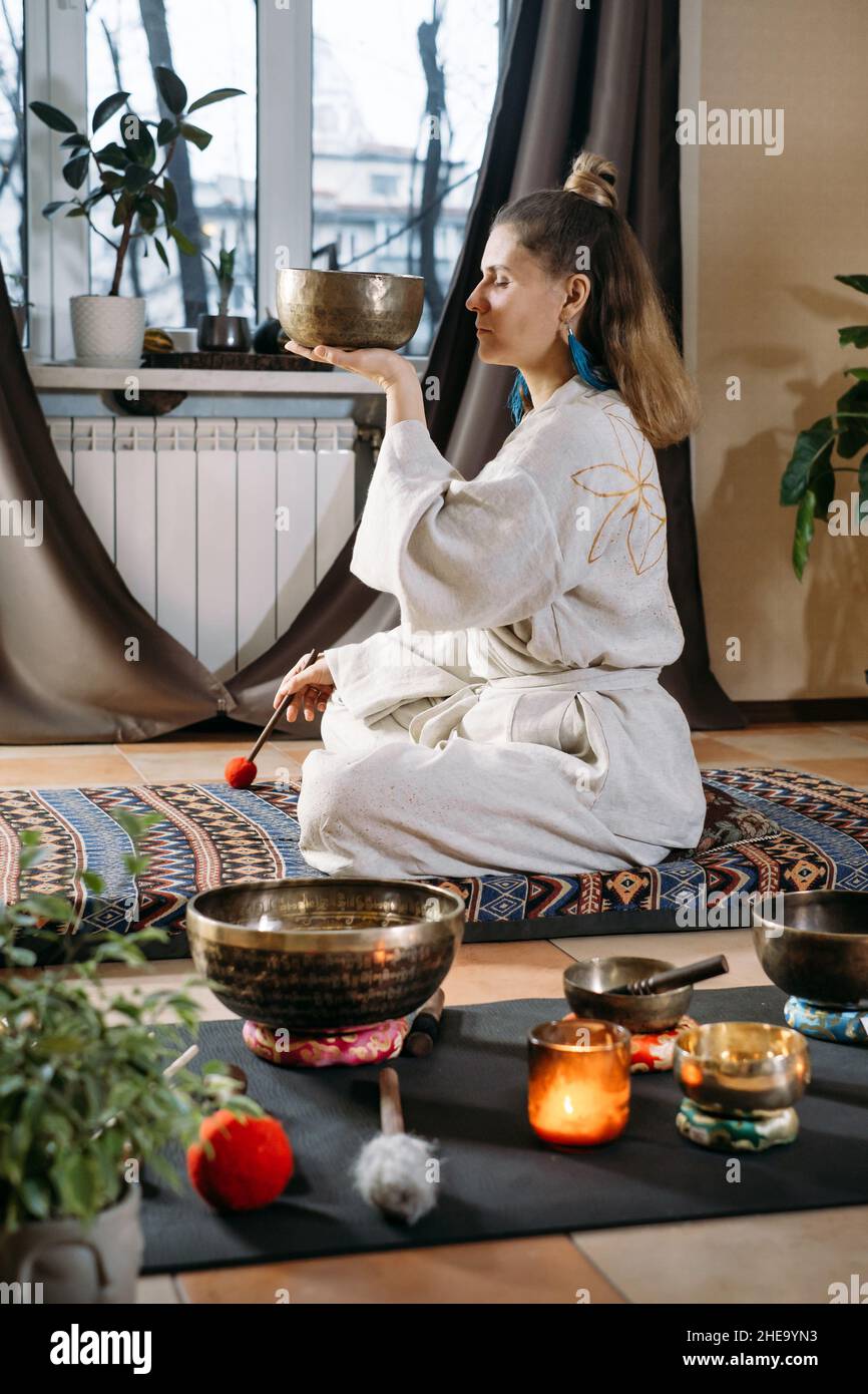 Sound healing with singing bowls, vibration massage and alternative treatment. Mental health care for adults. Woman in 40s playing to percussion Stock Photo
