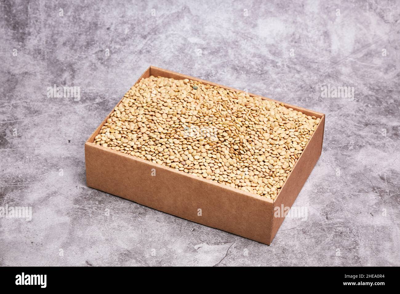 Cardboard box with dried green lentils on a gray stone background. Healthy and vegan food concept Stock Photo