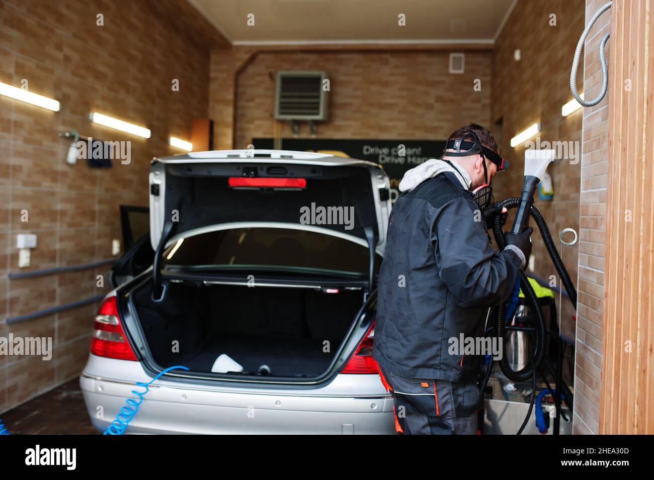 Man in uniform and respirator, worker of car wash center, cleaning car