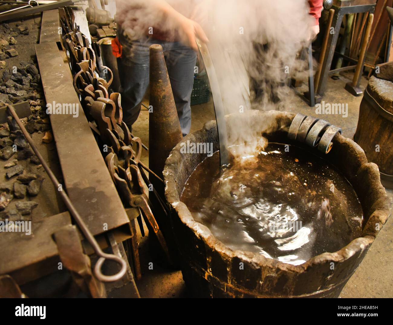 Leipzig, Germany. 16th Dec, 2021. Blacksmith's apprentice Claudia Süßmeyer dips a rod for a gate into a vat of water at the forge fire during machining. Artisan blacksmith Althammer, who founded his artisan forge 45 years ago, is delighted that his two daughters have taken over the craftsman's business and that he himself can provide advice based on his many years of experience. Credit: Waltraud Grubitzsch/dpa-Zentralbild/dpa/Alamy Live News Stock Photo