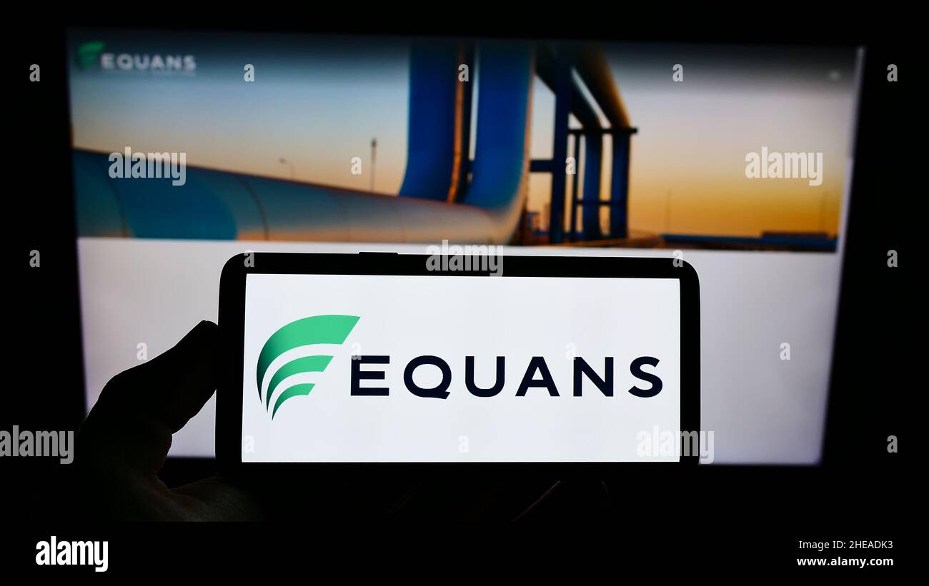 Person holding smartphone with logo of French facility management company EQUANS on screen in front of website. Focus on phone display. Stock Photo