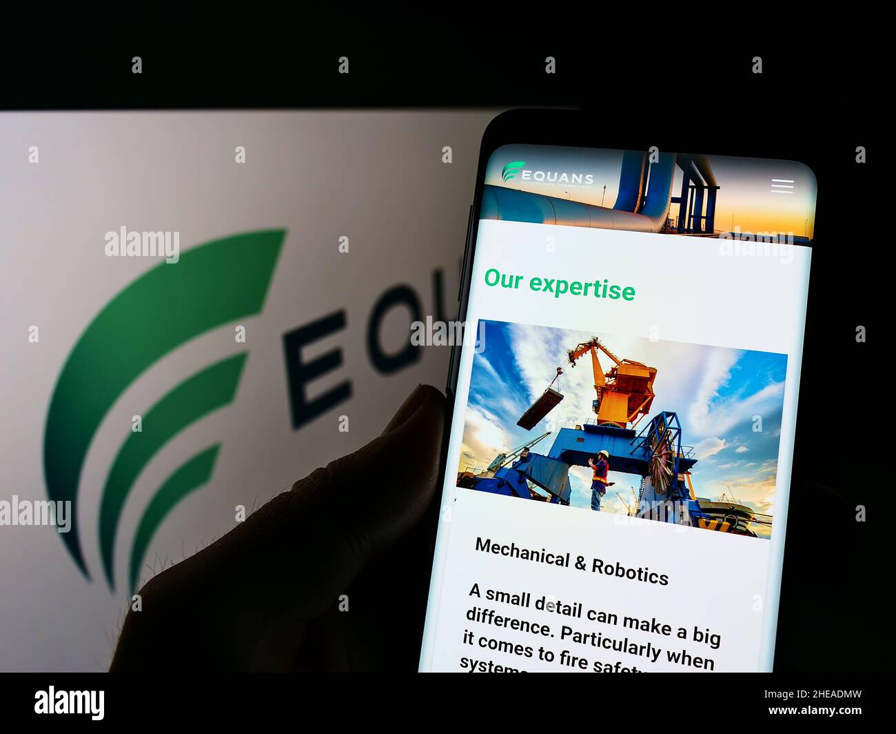 Person holding cellphone with website of French facility management company EQUANS on screen in front of logo. Focus on center of phone display. Stock Photo