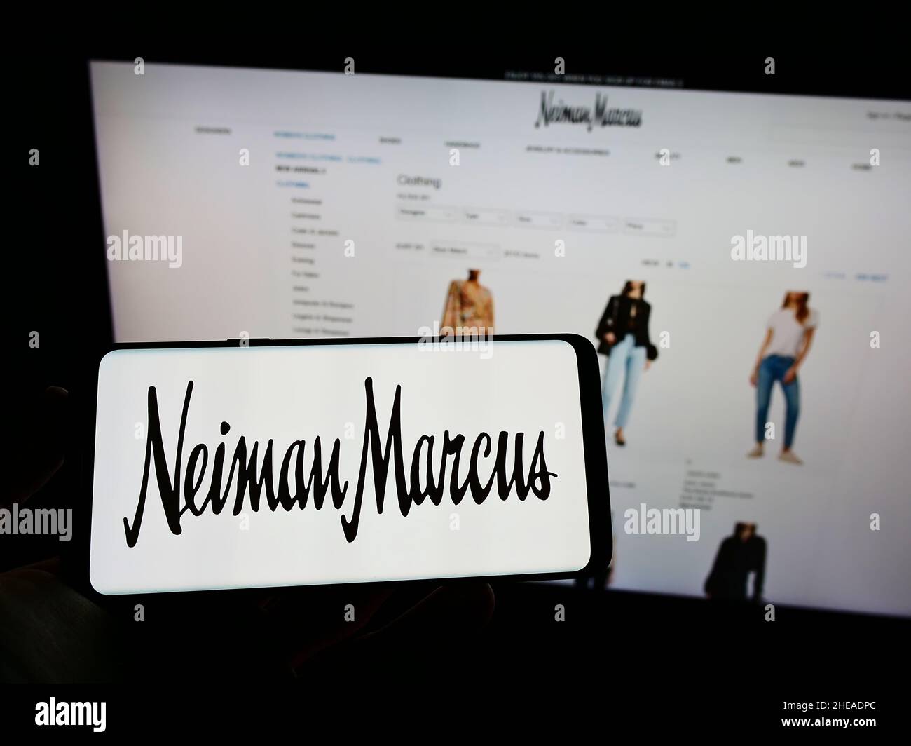 Person holding mobile phone with logo of American luxury retailer Neiman Marcus Group Inc. on screen in front of web page. Focus on phone display. Stock Photo