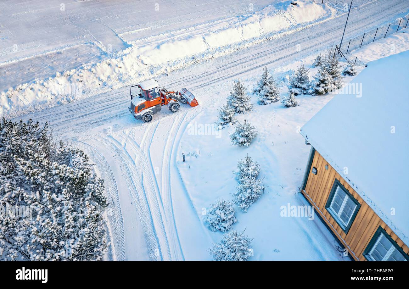 Snow removing with red tractor on the road. Suny winter day, Drone top view. Aerial. View from above. Stock Photo
