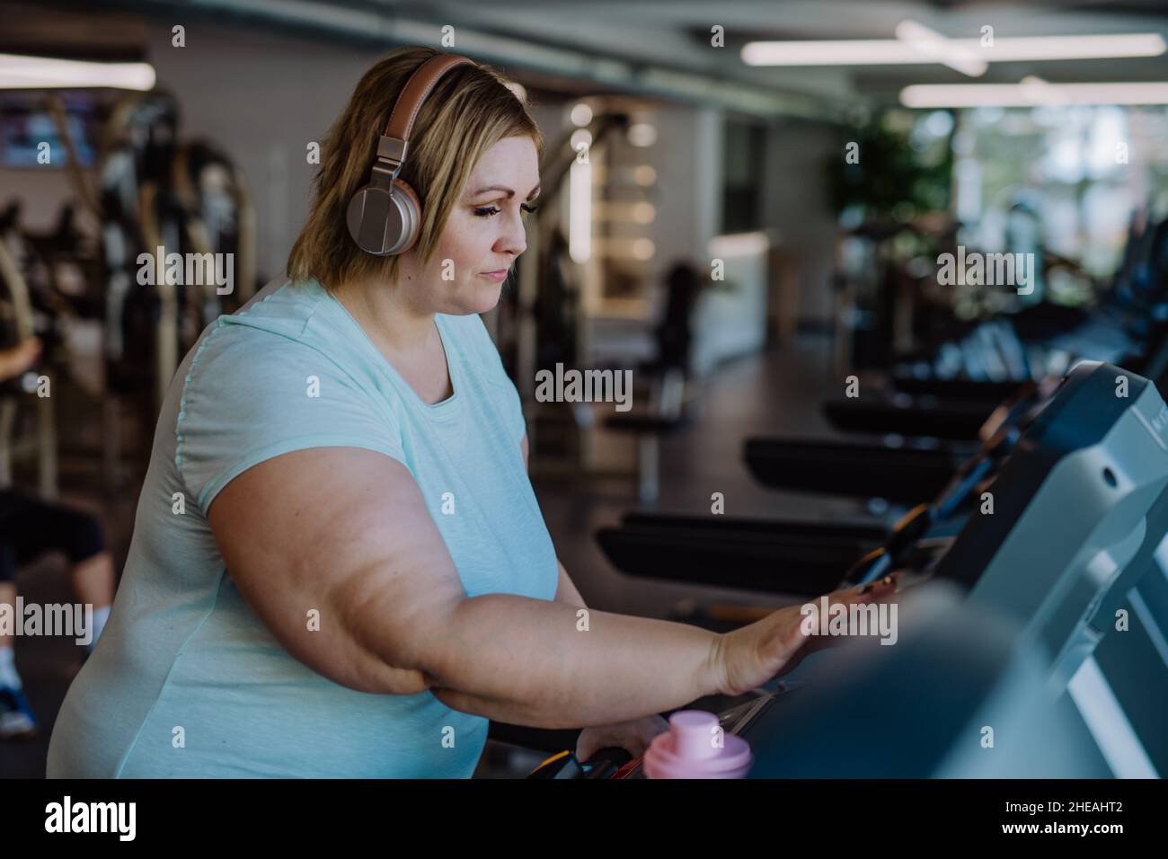 Mid adult overweight woman with headphones exercising on treadmill in gym Stock Photo