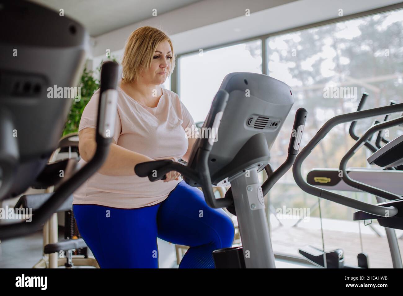 Happy mid adult overweight woman exercising on stepper indoors in gym Stock Photo