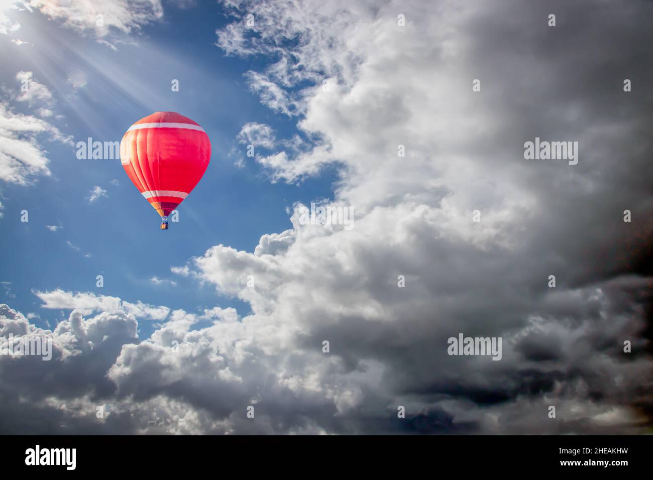 a red hot air balloon soaring into clouds of a summer storm Stock Photo