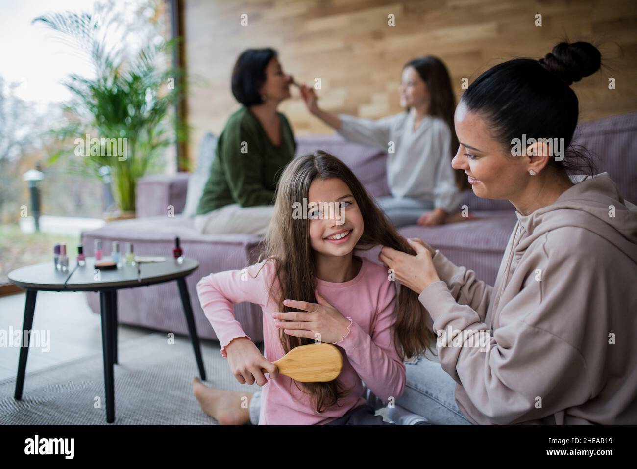 Two happy sisters with mother and grandmother combing hair and doing make up together at home Stock Photo