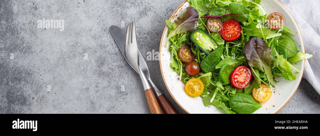 Vegetables healthy salad with red and yellow cherry tomatoes, pepper and green salad leafs on white rustic ceramic plate Stock Photo