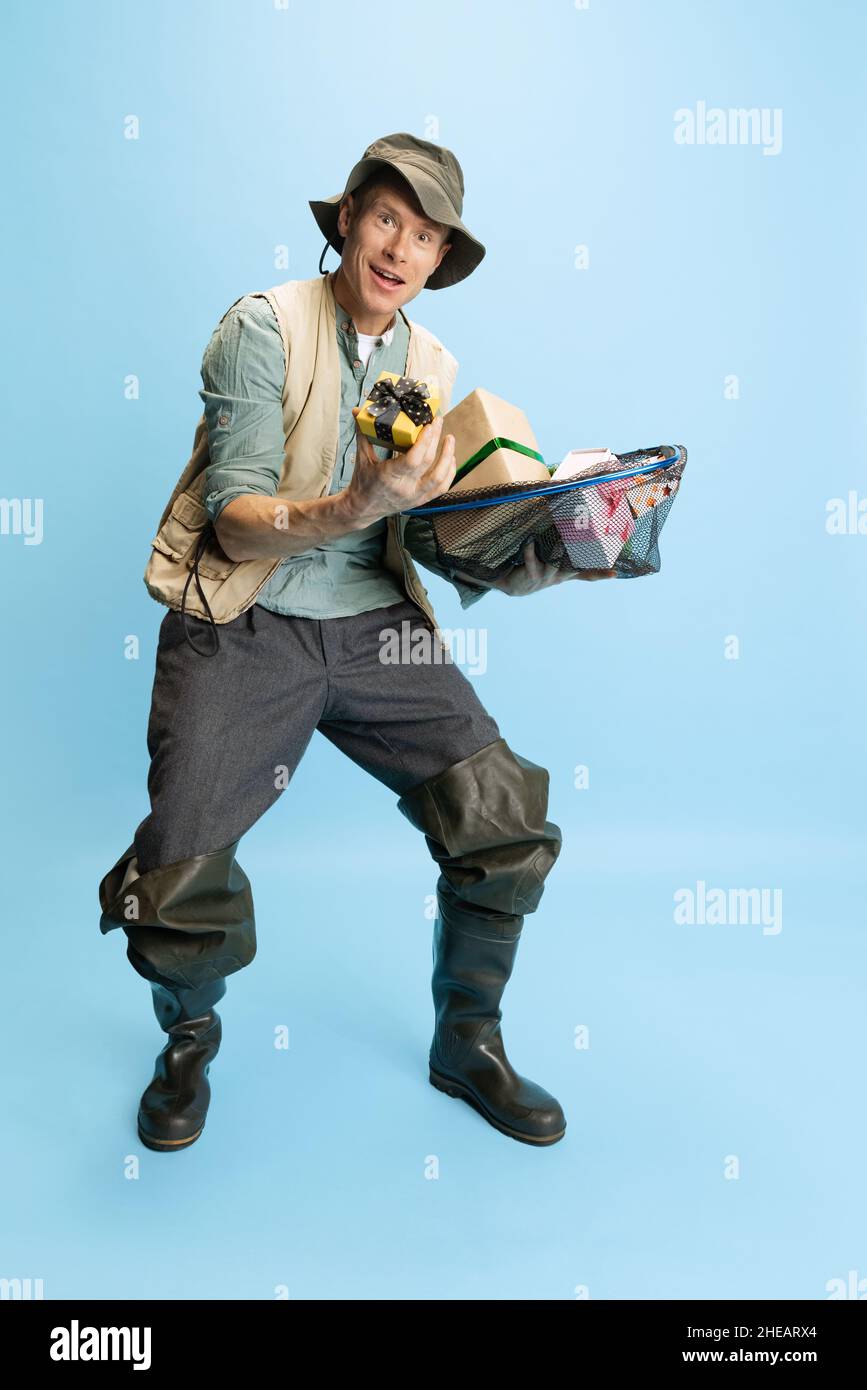 Funny young man, fisherman with fishing accessories wearing sport style  clothes isolated over blue studio background Stock Photo - Alamy