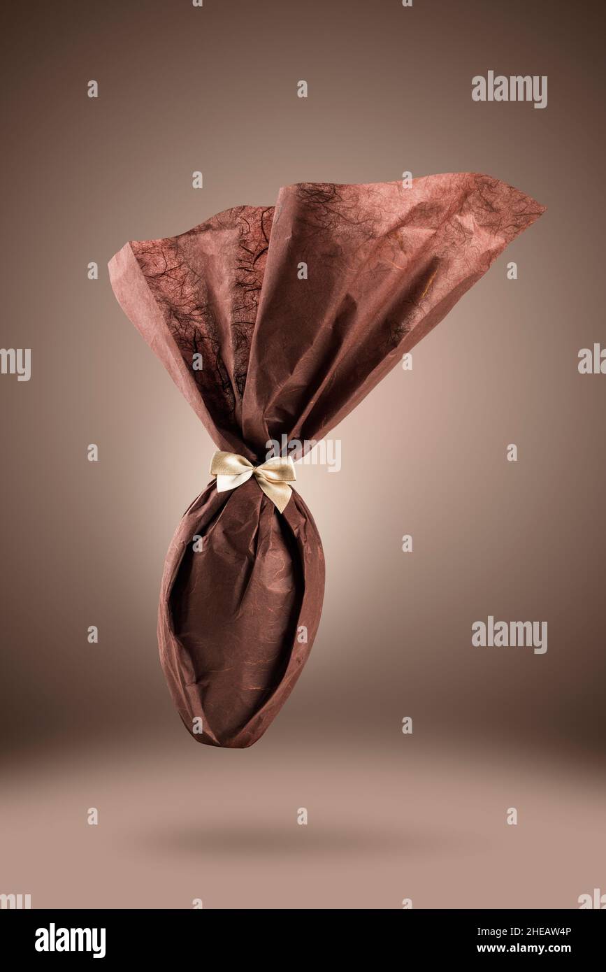 Chocolate easter egg packed with elegant brown paper on brown background Stock Photo