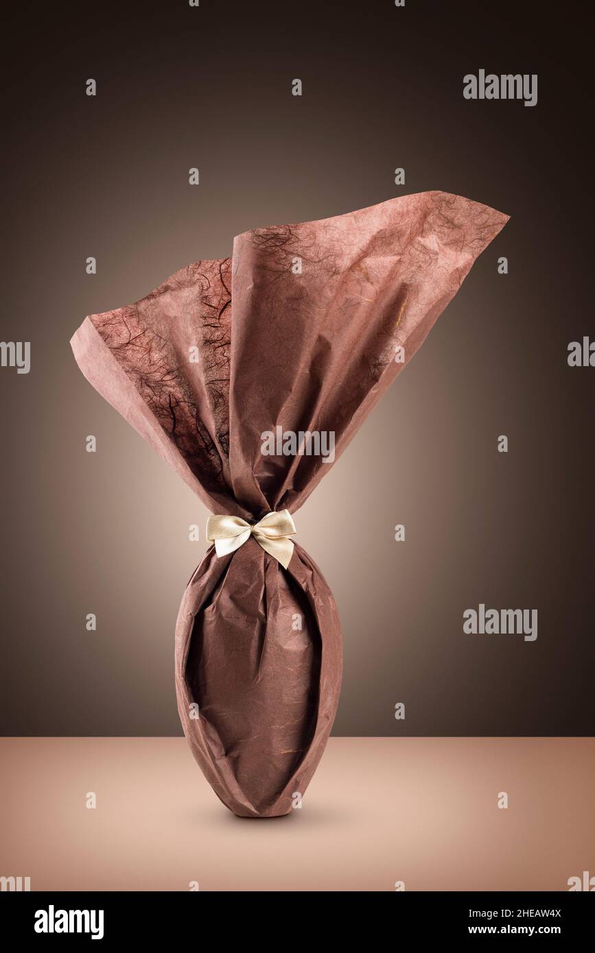 Chocolate easter egg packed with elegant brown paper on brown background Stock Photo
