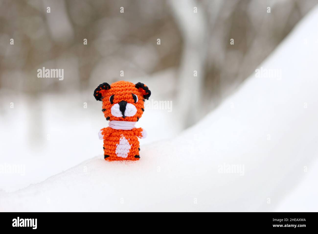 Knitted toy tiger in snow in a forest. Background for greeting card of New Year celebration, Year 2022 of the tiger according to the Chinese calendar Stock Photo