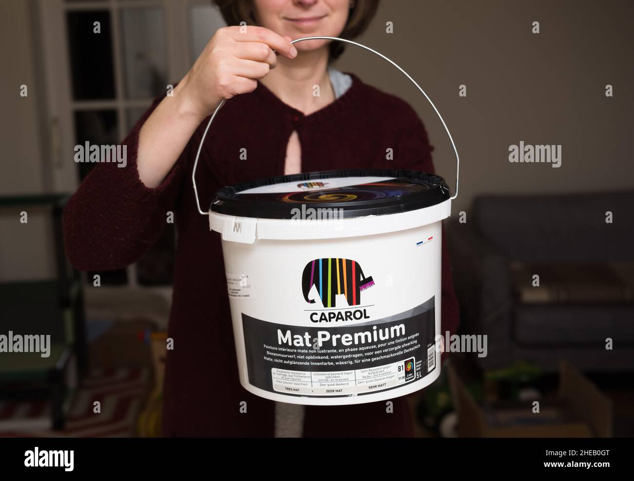 Paris, France - Dec 8, 2021: Young woman holding new plastic package bucket of Caparol Mat Premium luxury German paint Stock Photo