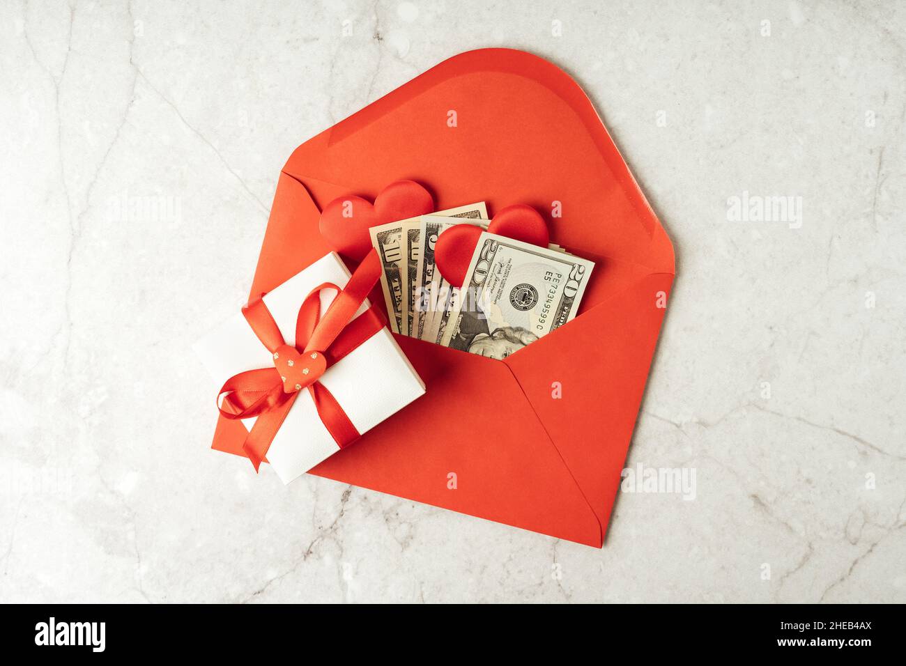 Red paper envelope with money dollars bills. Flat lay of gray working table background with Valentine gift, letter, heart shape. Top view, mock up Stock Photo