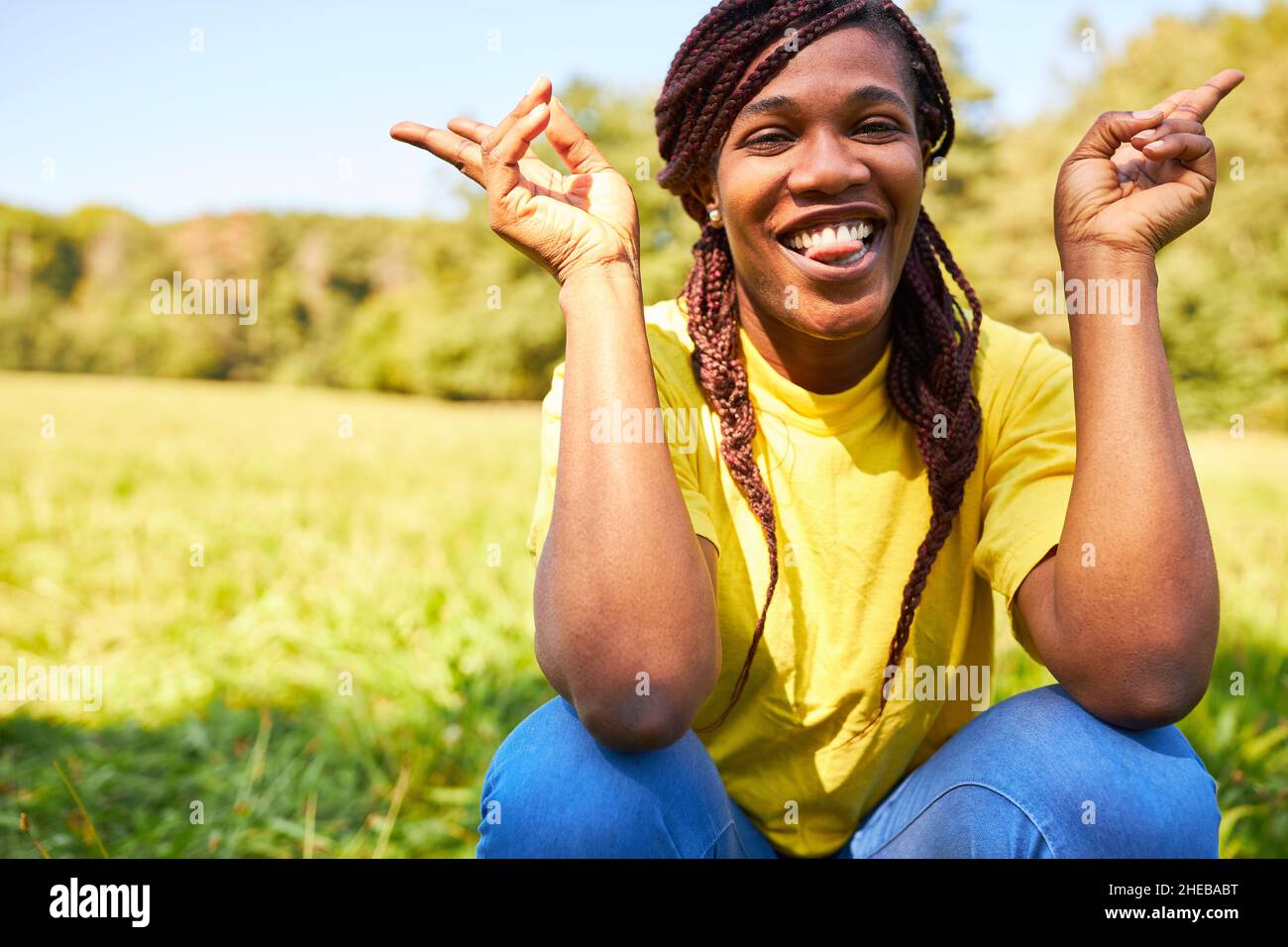 Confident young woman with Rasta braids on a meadow in summer with cool gestures Stock Photo