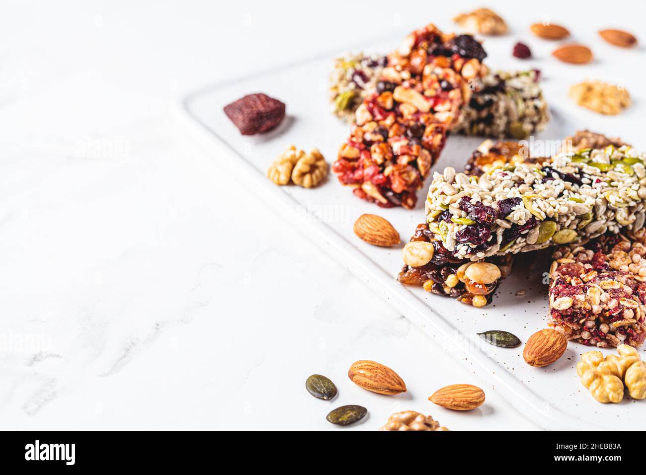 Energy granola bars with different seeds, nuts and dried fruits and berries on a white marble background, copy space. Healthy snack concept. Stock Photo