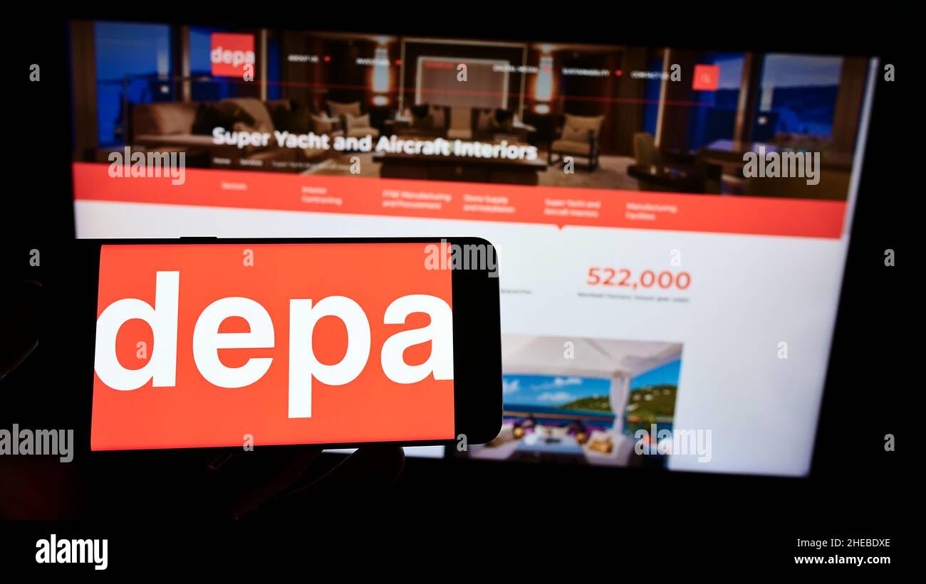 Person holding cellphone with logo of interior construction company Depa Plc on screen in front of business webpage. Focus on phone display. Stock Photo
