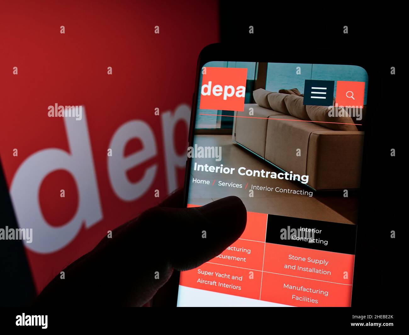 Person holding cellphone with webpage of interior construction company Depa Plc on screen in front of logo. Focus on center of phone display. Stock Photo