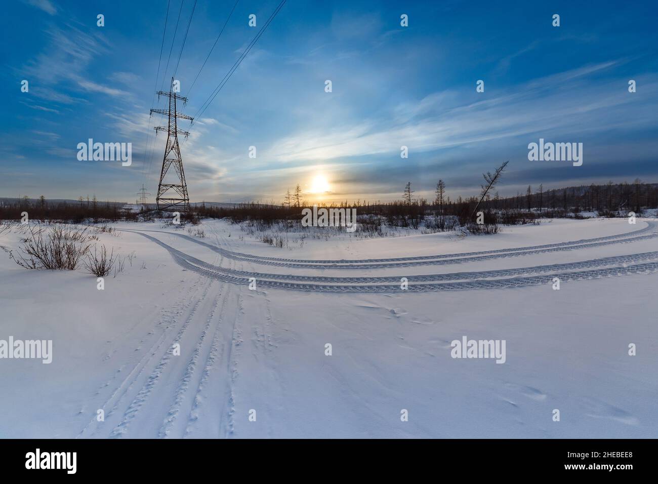 Evening winter landscape with power transmission towers and traces from a car in South Yakutia, Russia Stock Photo