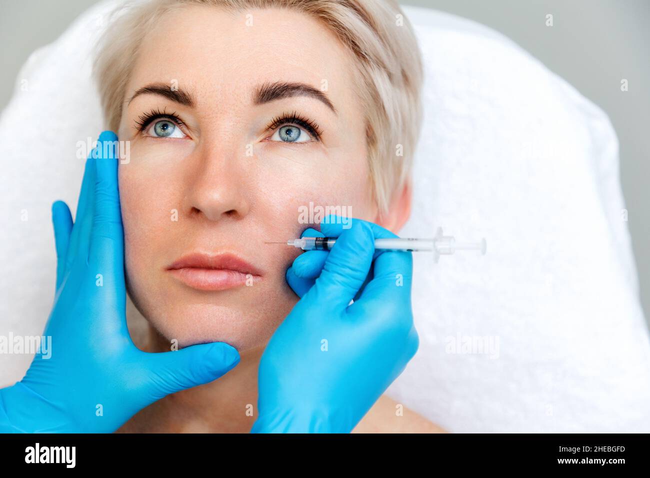 Beautician in medical gloves with syringe injects filler in nasolabial fold. Close-up portrait of beautiful adult woman getting injection in the cosme Stock Photo