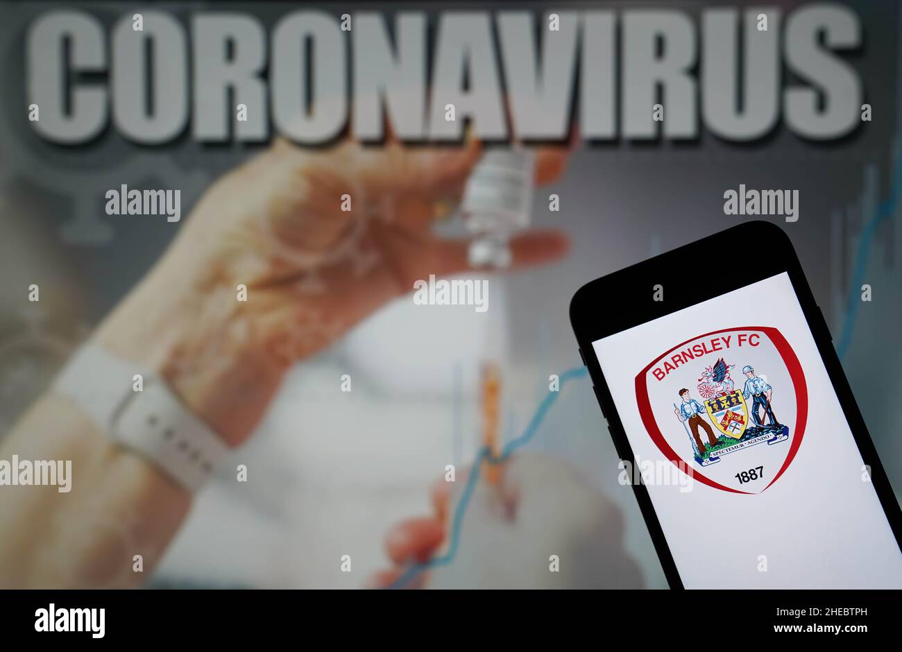 File photo dated 09-01-2021 of The Barnsley Football Club logo seen displayed on a mobile phone with a Coronavirus illustration on a monitor in the background. The Sky Bet Championship game between Barnsley and Stoke at Oakwell on Wednesday has been postponed due to the number of injuries and positive Covid-19 cases within the Barnsley camp. Issue date: Monday January 10, 2022. Stock Photo