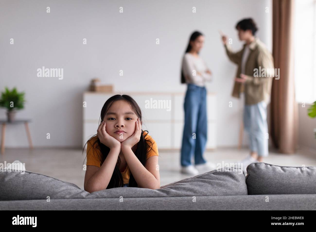 Sad youngsters girl looks at camera, young asian couple quarreling at home in living room interior Stock Photo