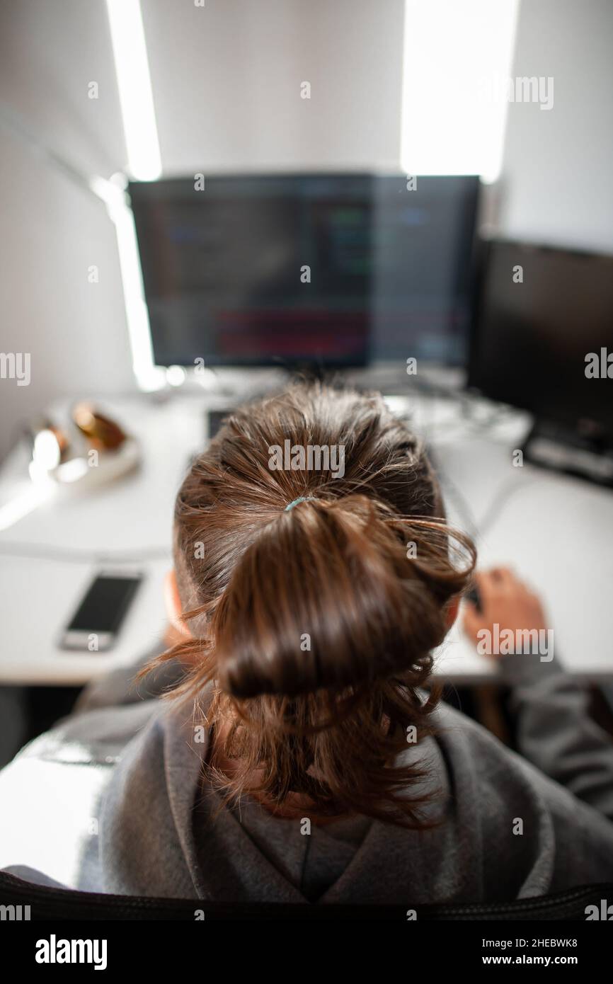 Man in front of two computers back view | Young caucasian man with long hair with man bun use computer with two monitors and laptop Stock Photo