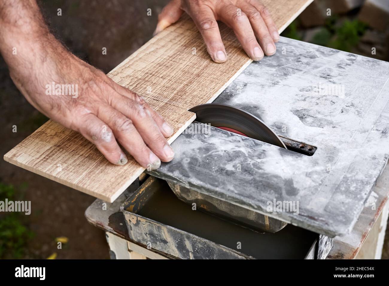 A man cuts a ceramic tile using a tile cutter with water cooled. Close-up, selective focus Stock Photo